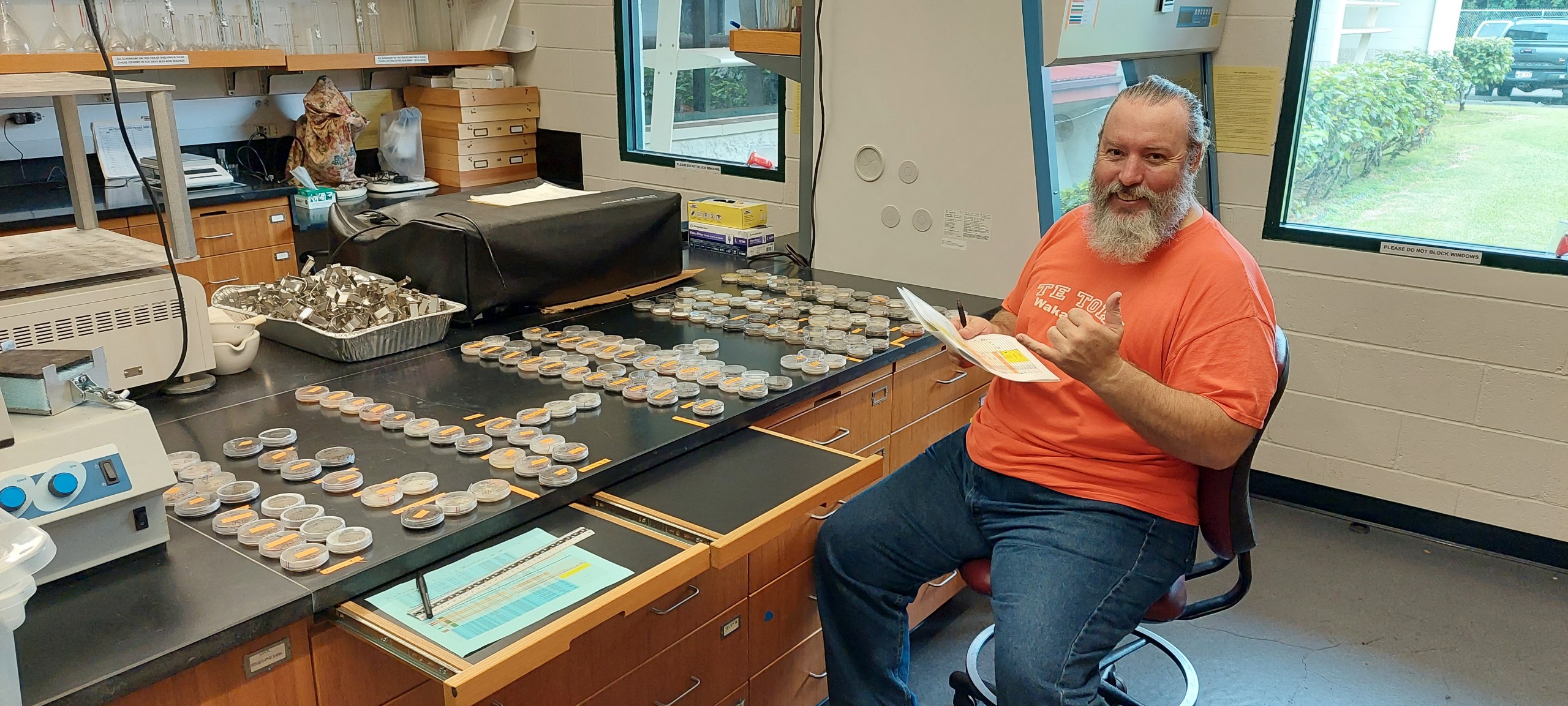Sean throws a shaka in the lab with dozens of petri dishes sitting on the lab bench
