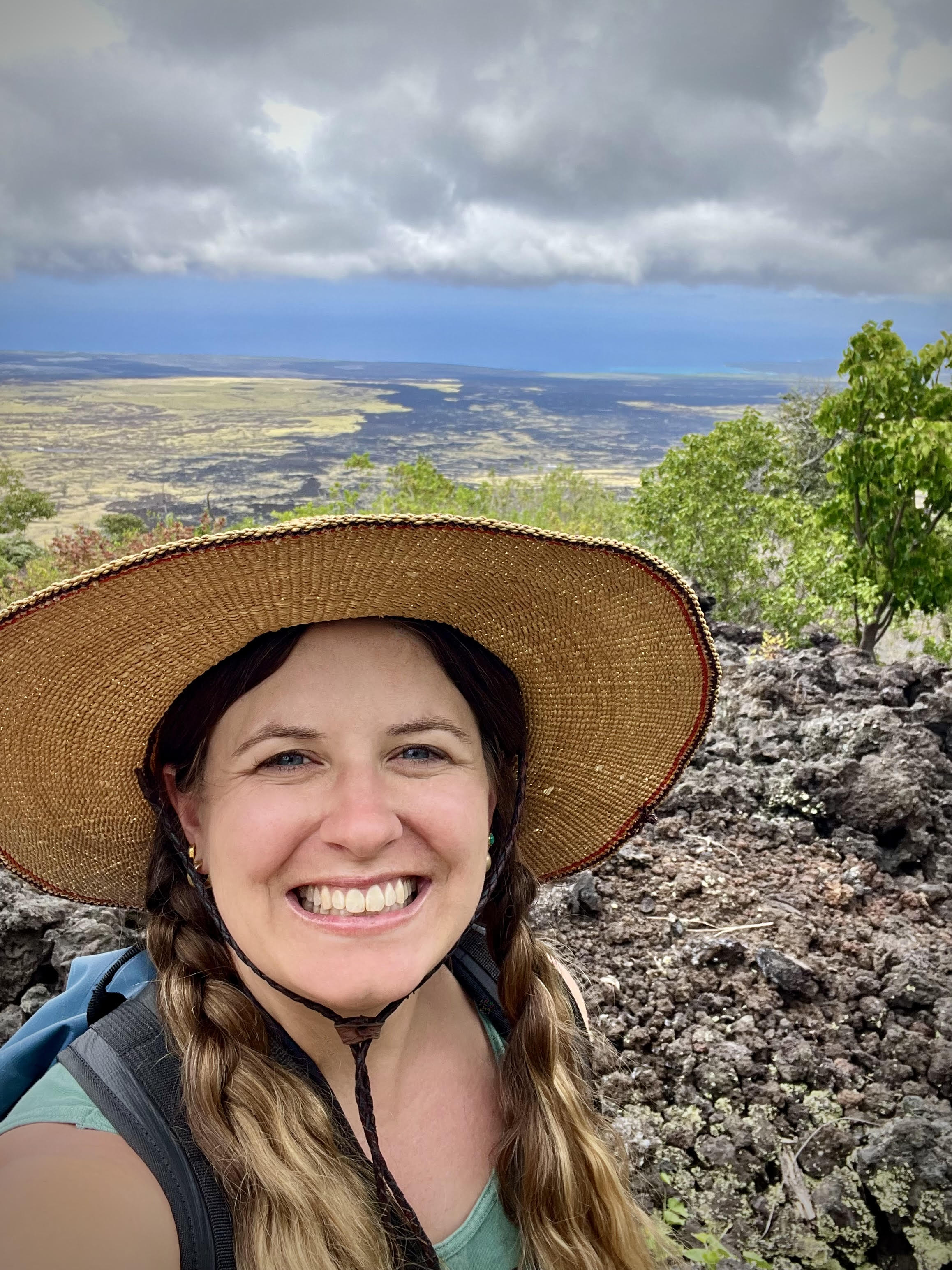 Selfie of Hannah wearing a sunhat while walking over an older lava flow