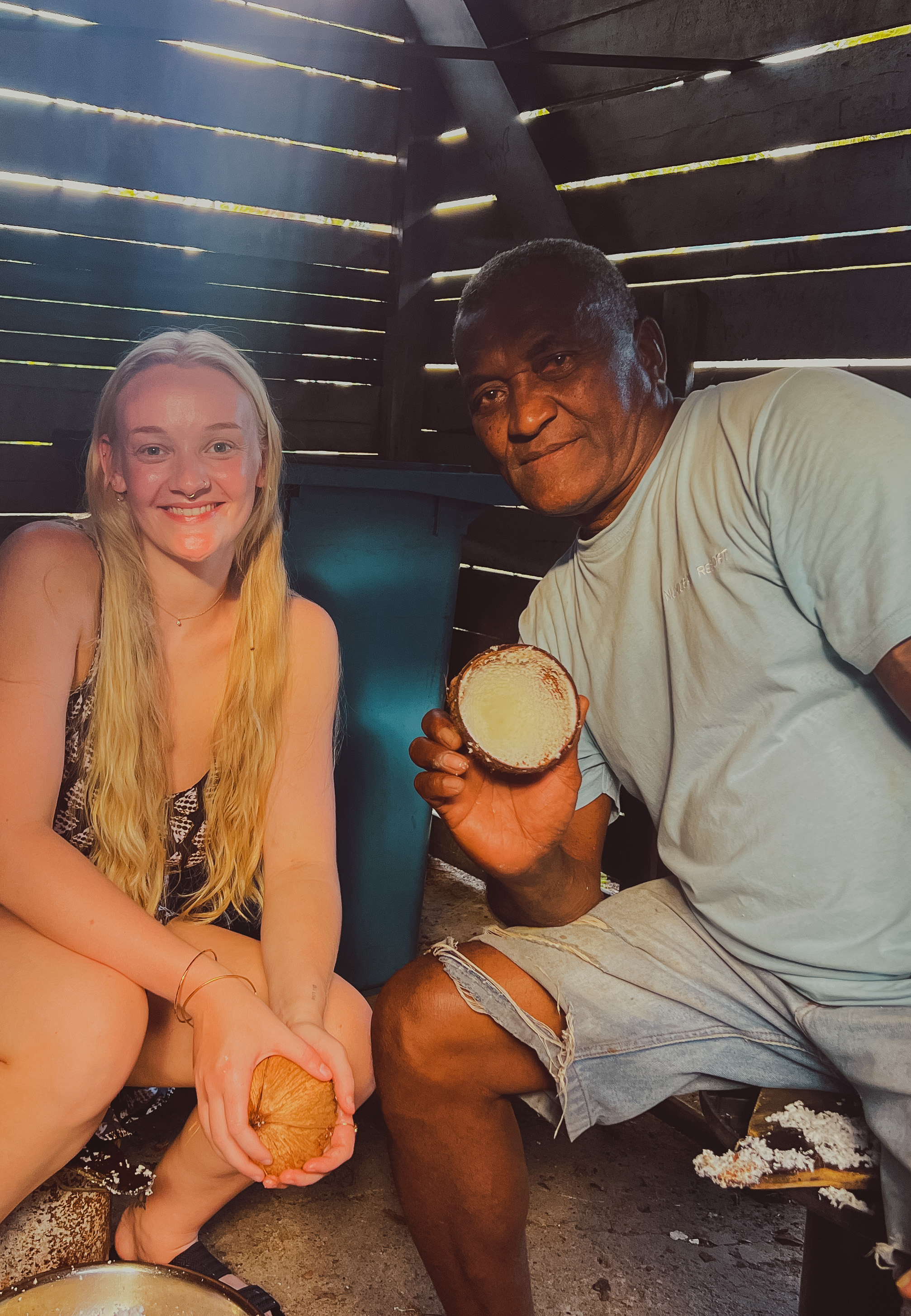 Sibley and a man hold open coconuts at a house in Fiji