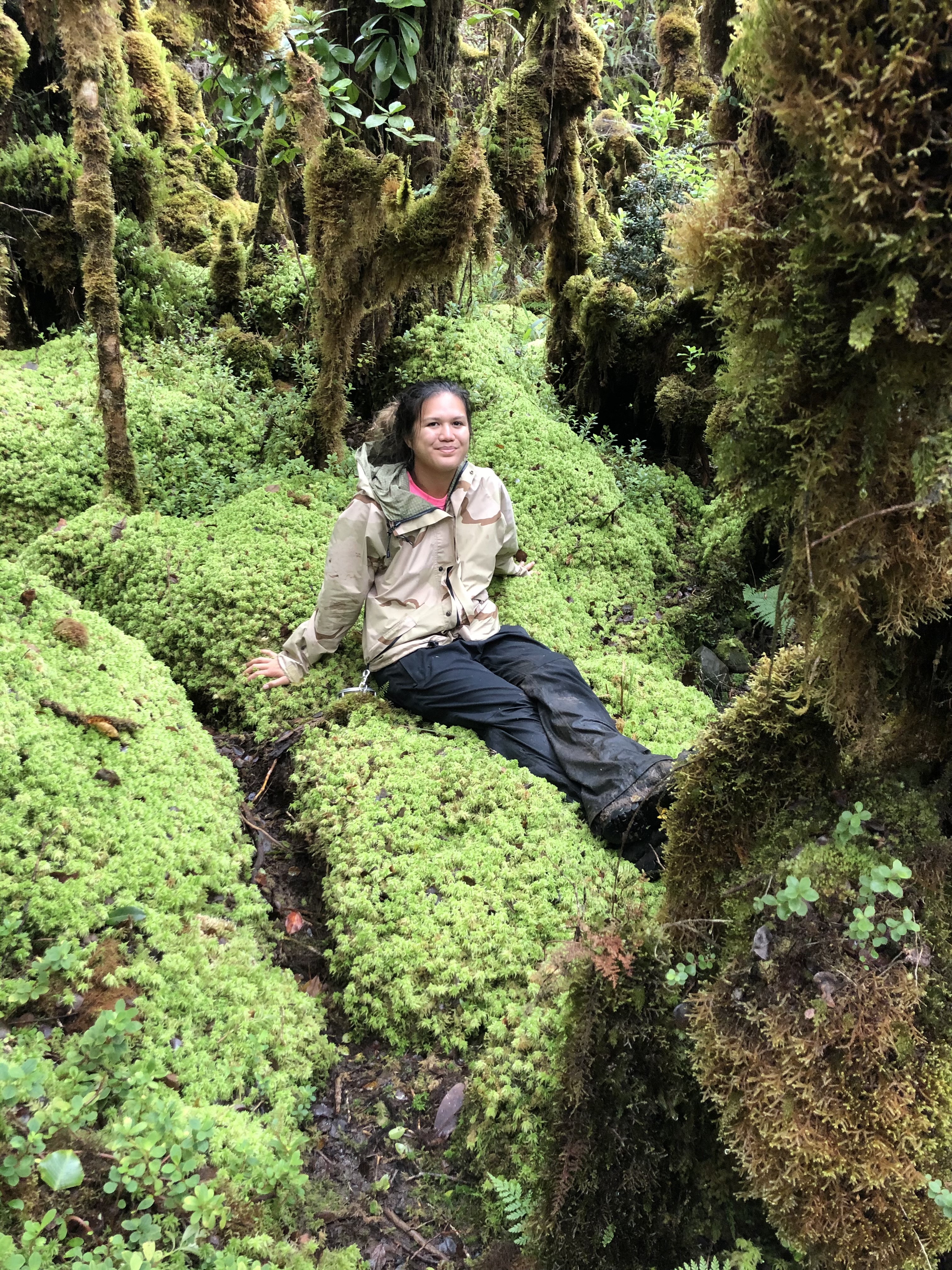 Kalena sits on a bed of moss in a native Hawaiian forest