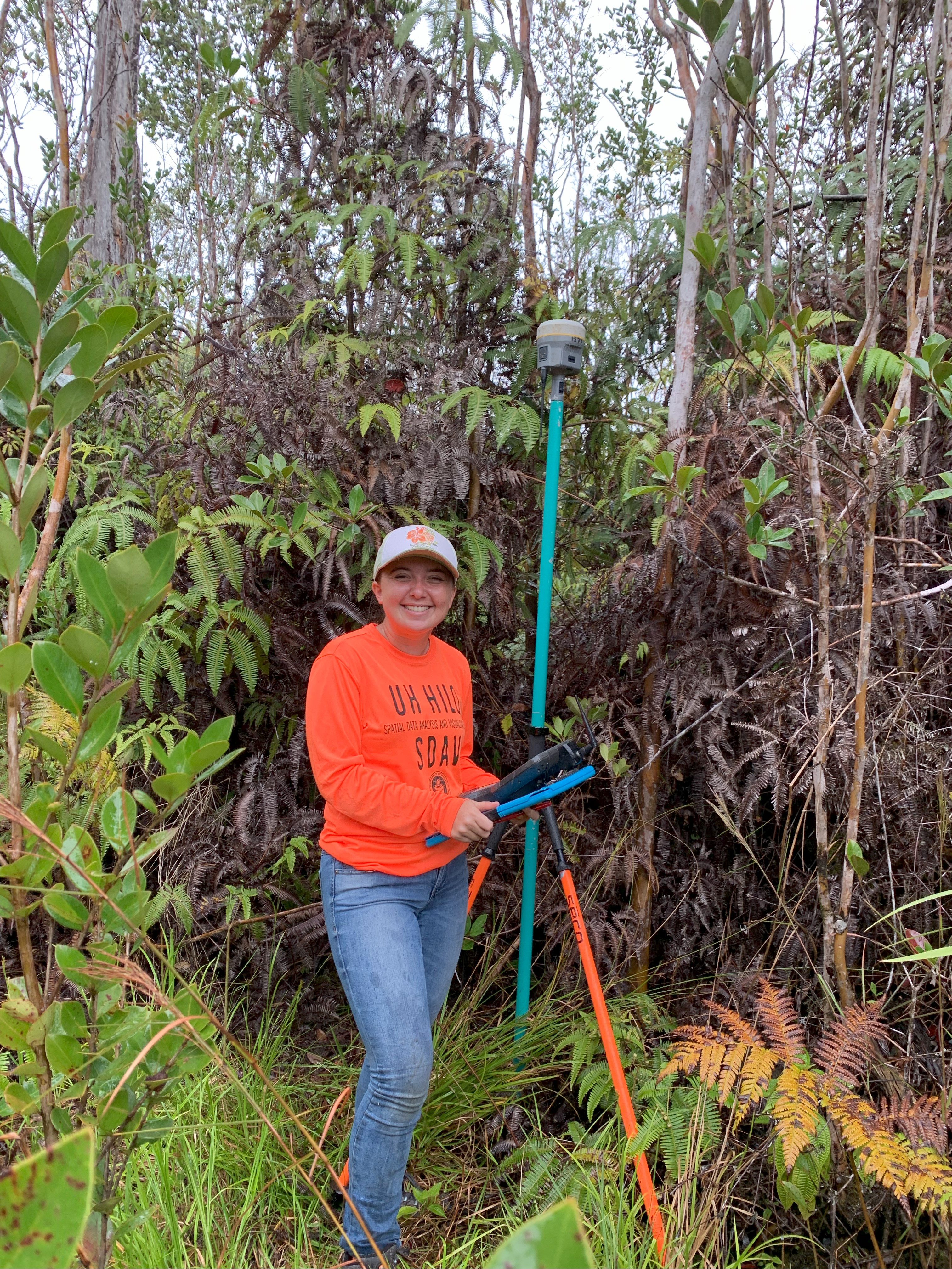Olivia stands in a native forest next to a tall piece of remote sensing equipment