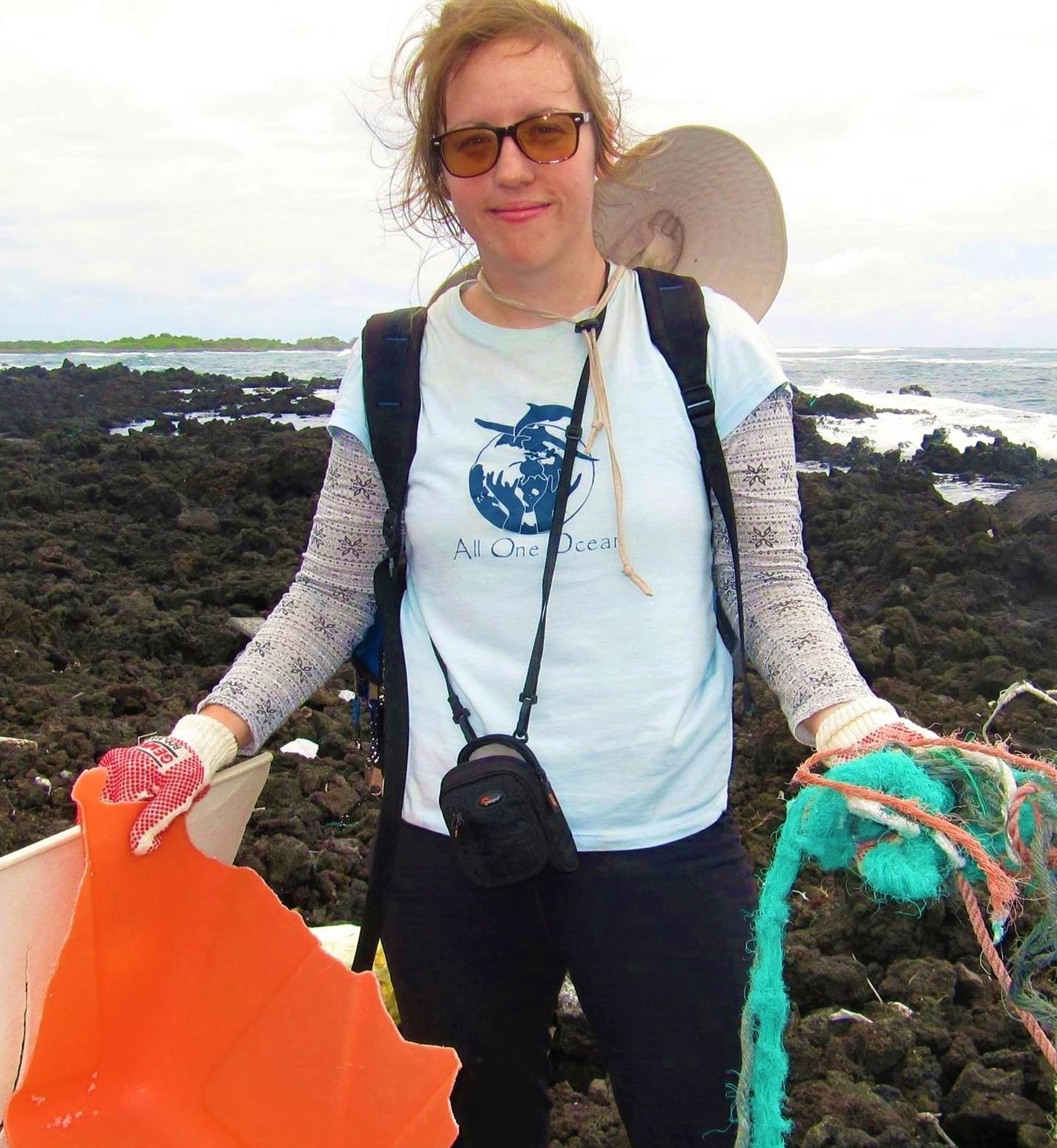 Young woman with red hair stands on the beach holding marine debris