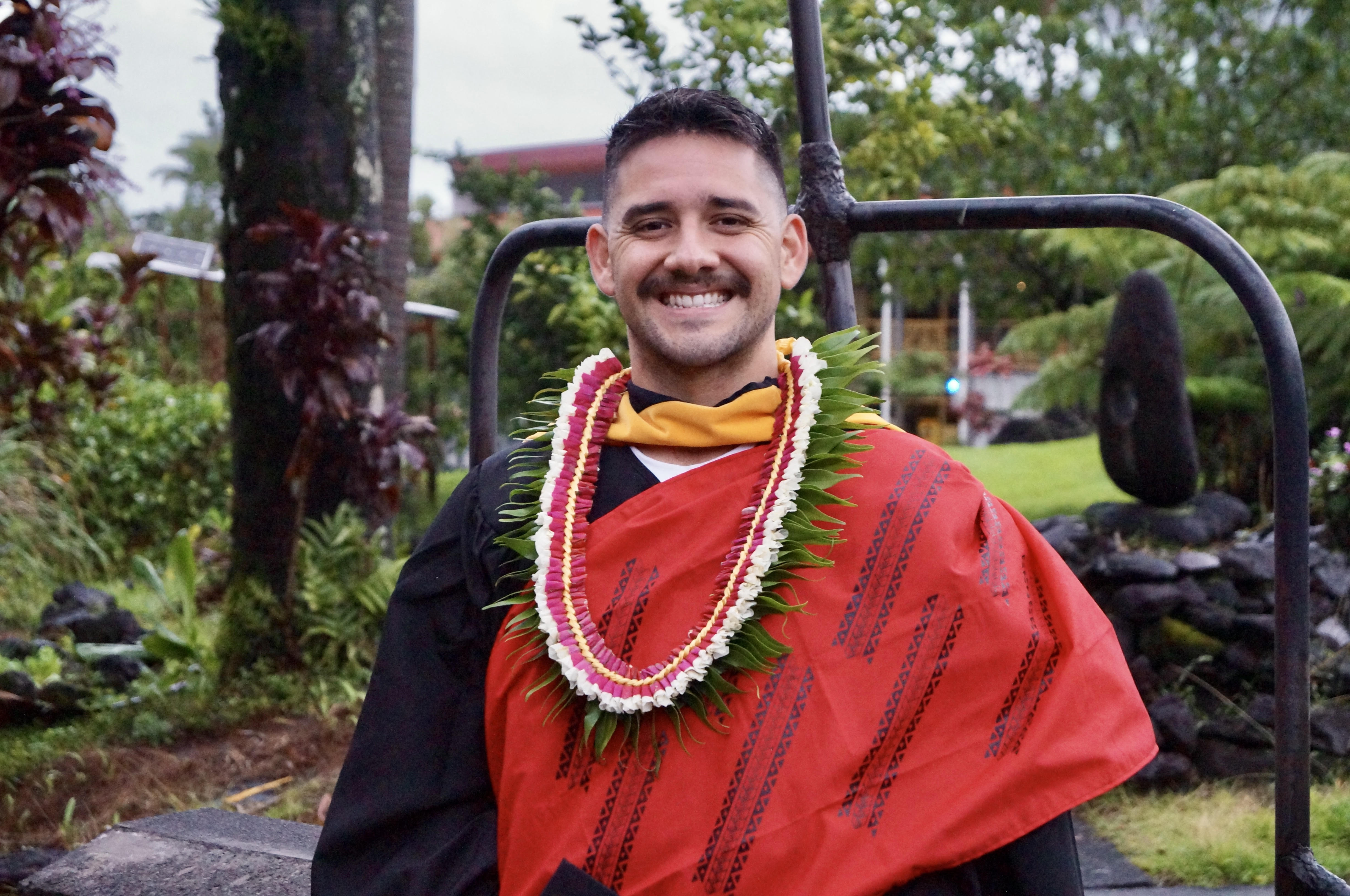 Young man smiling in graduation robes with a lei around his neck