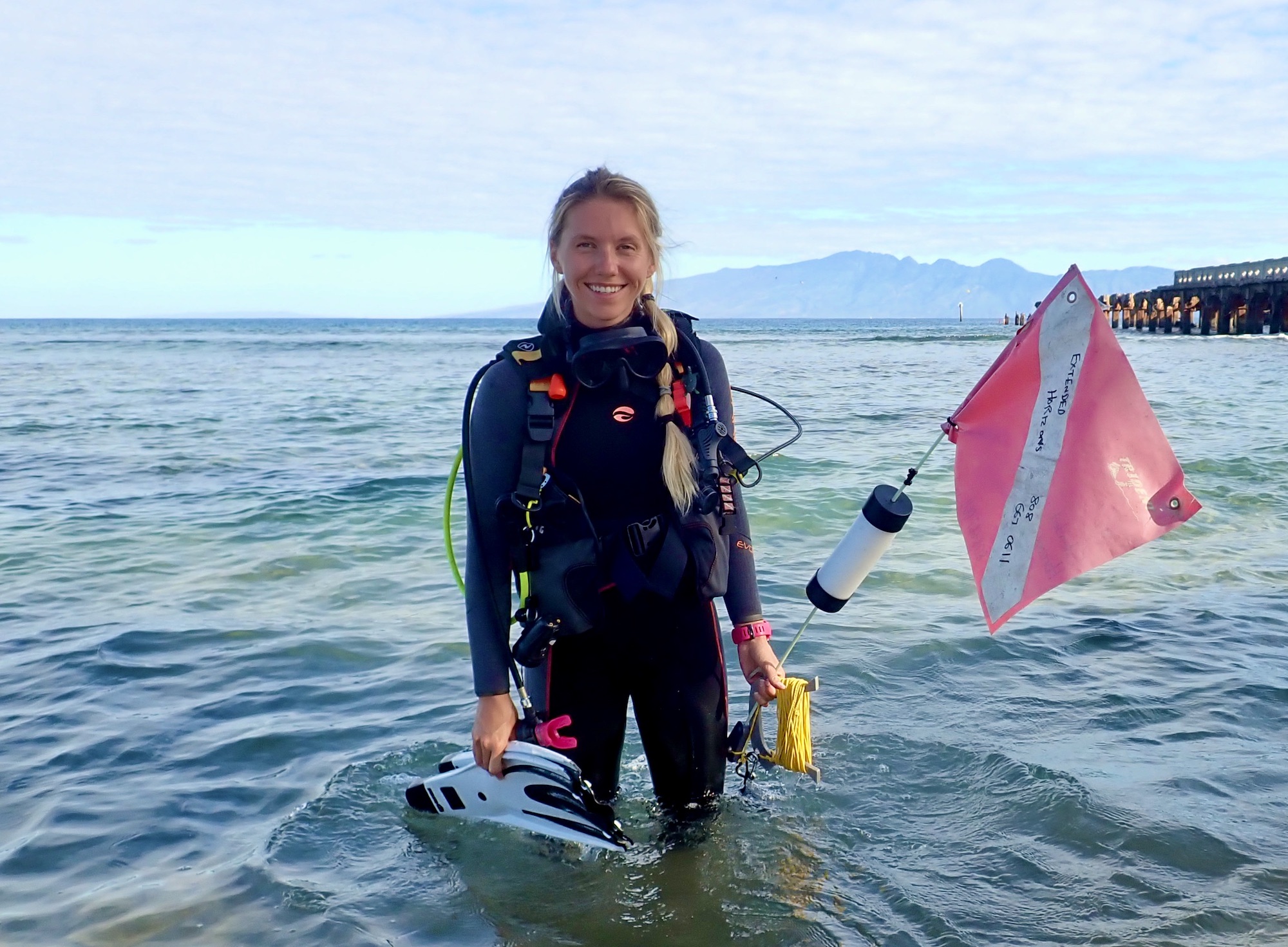 Jessica stands in the ocean wearing and carrying dive gear