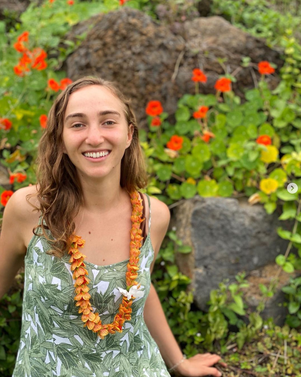 Headshot of Anna donning a lei and standing in front of red flowers