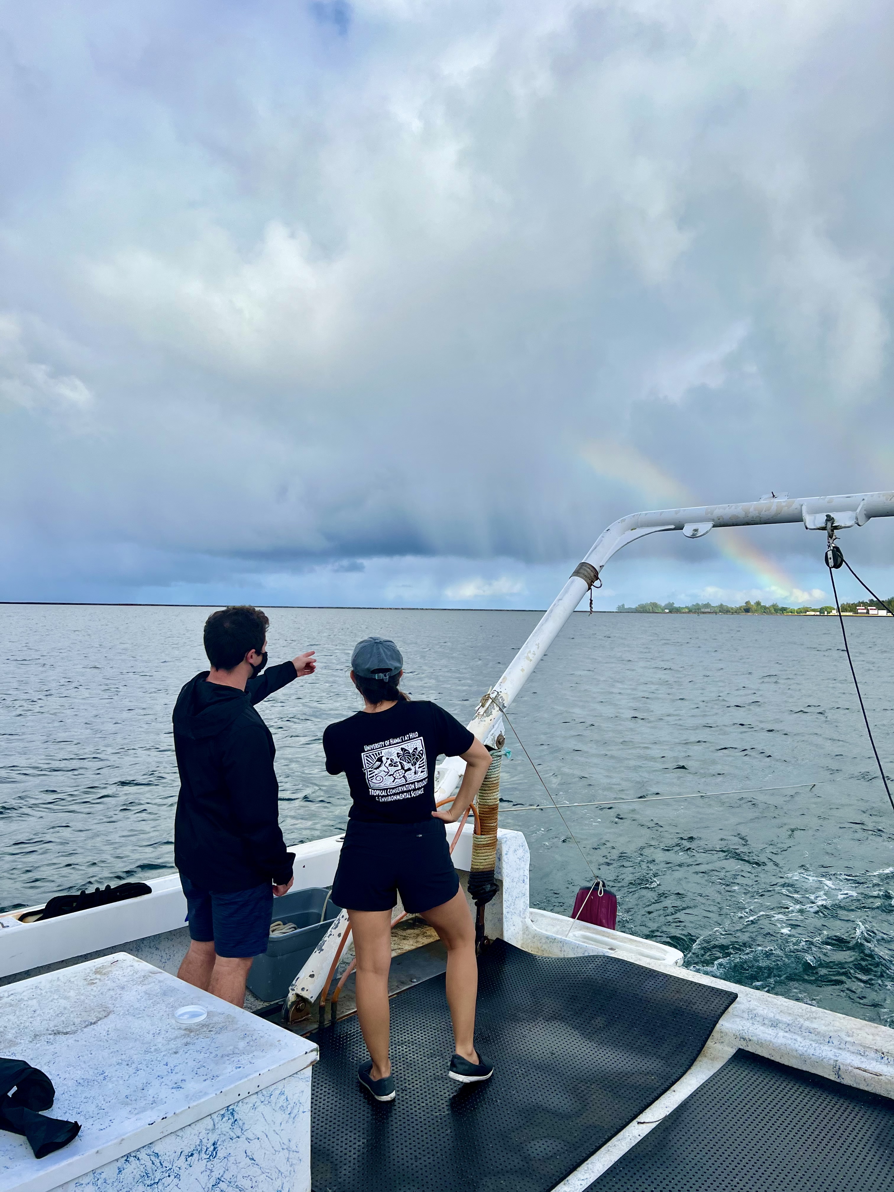 Dawn and colleague stand on a boat and look out at a rainbow over the water