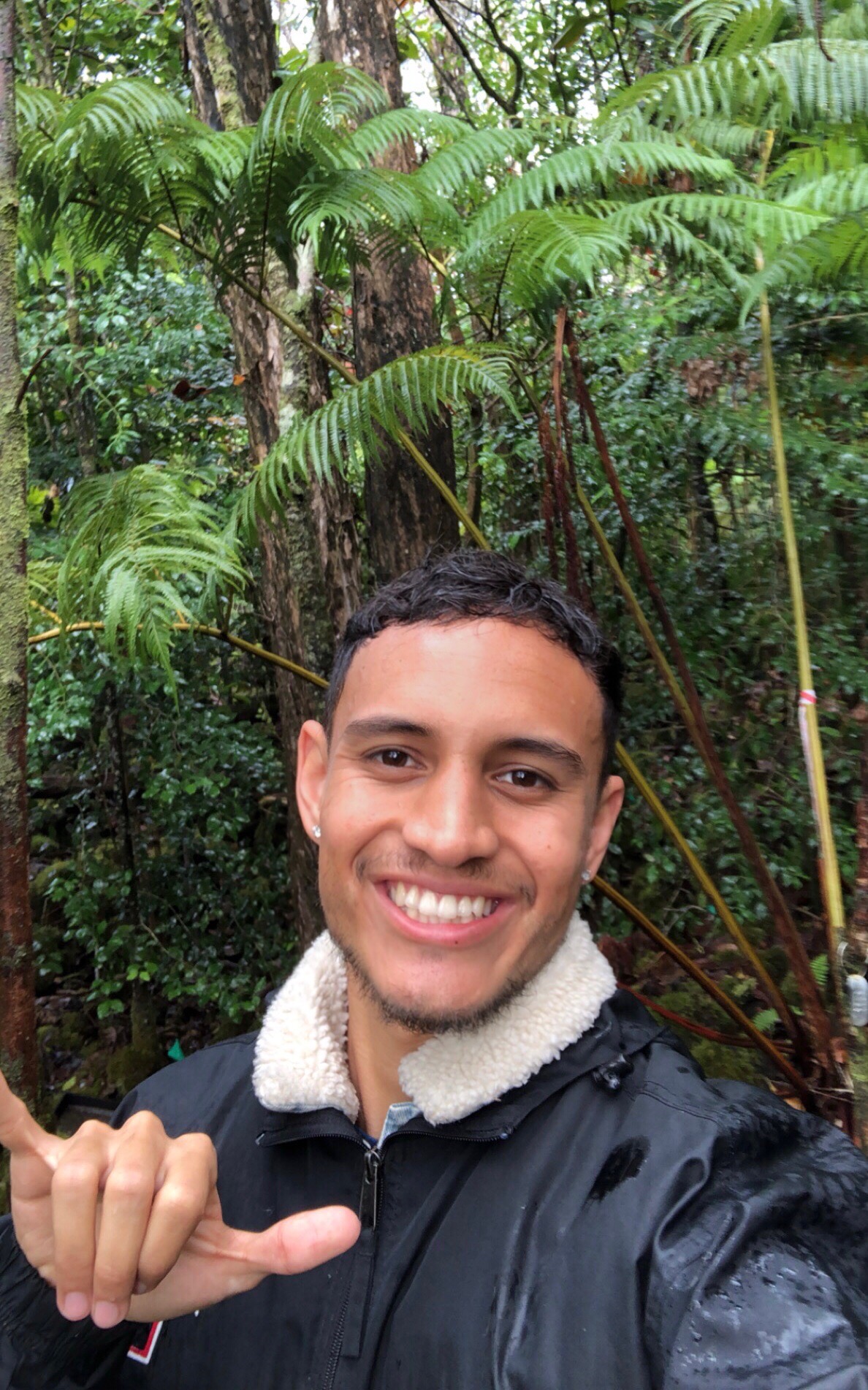 Kūpono throws a shaka while taking a selfie in a forest