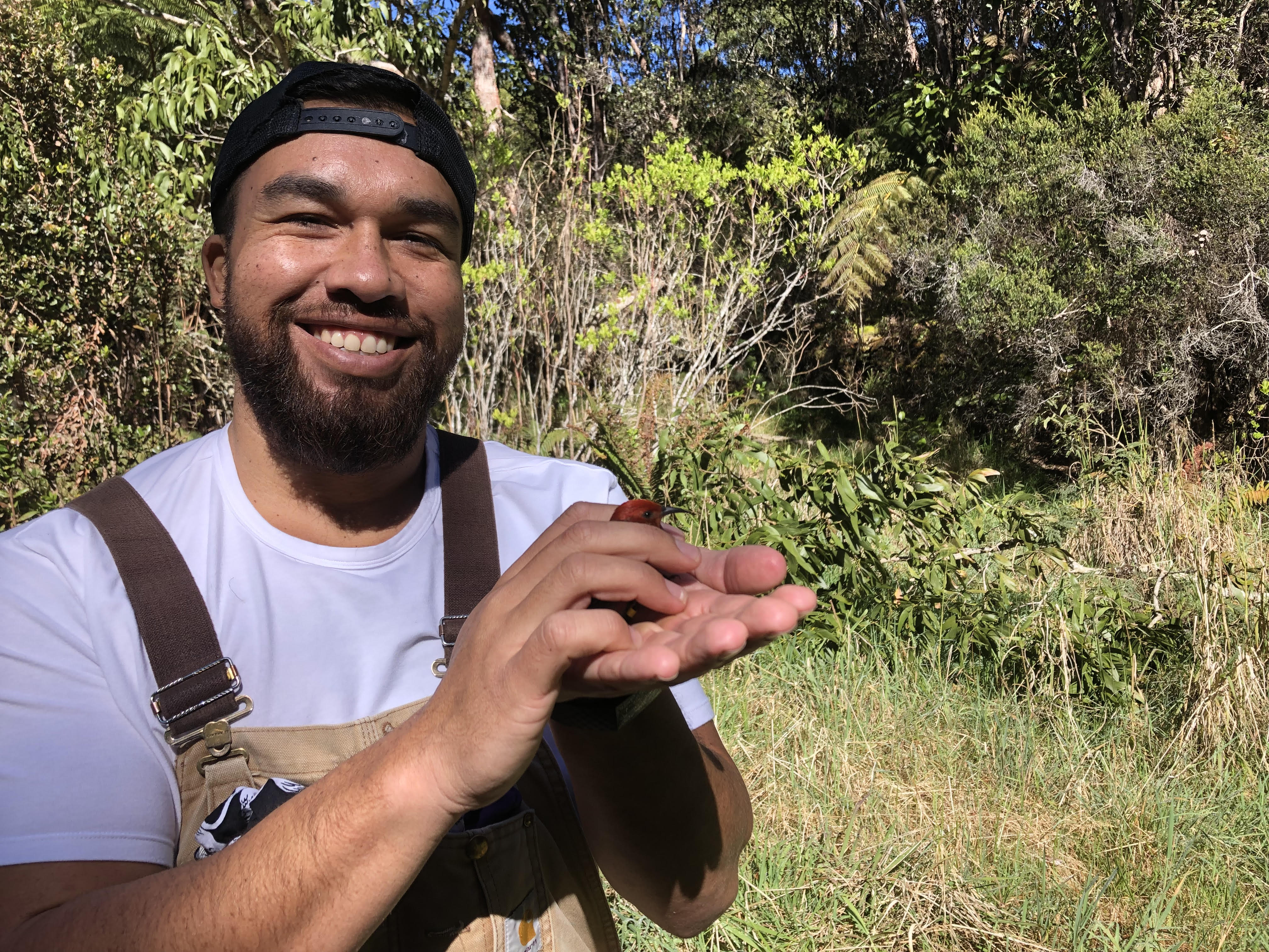 Robert in the field smiling and holding an 'apapane